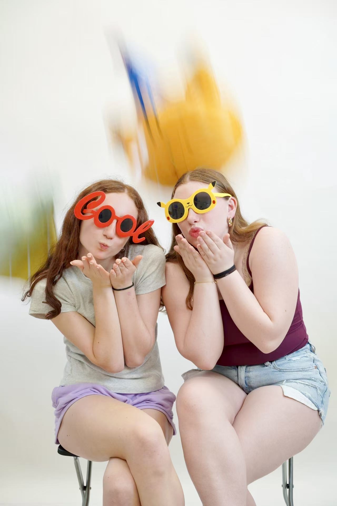 Two friends in playful sunglasses blowing kisses during a half-body portrait session