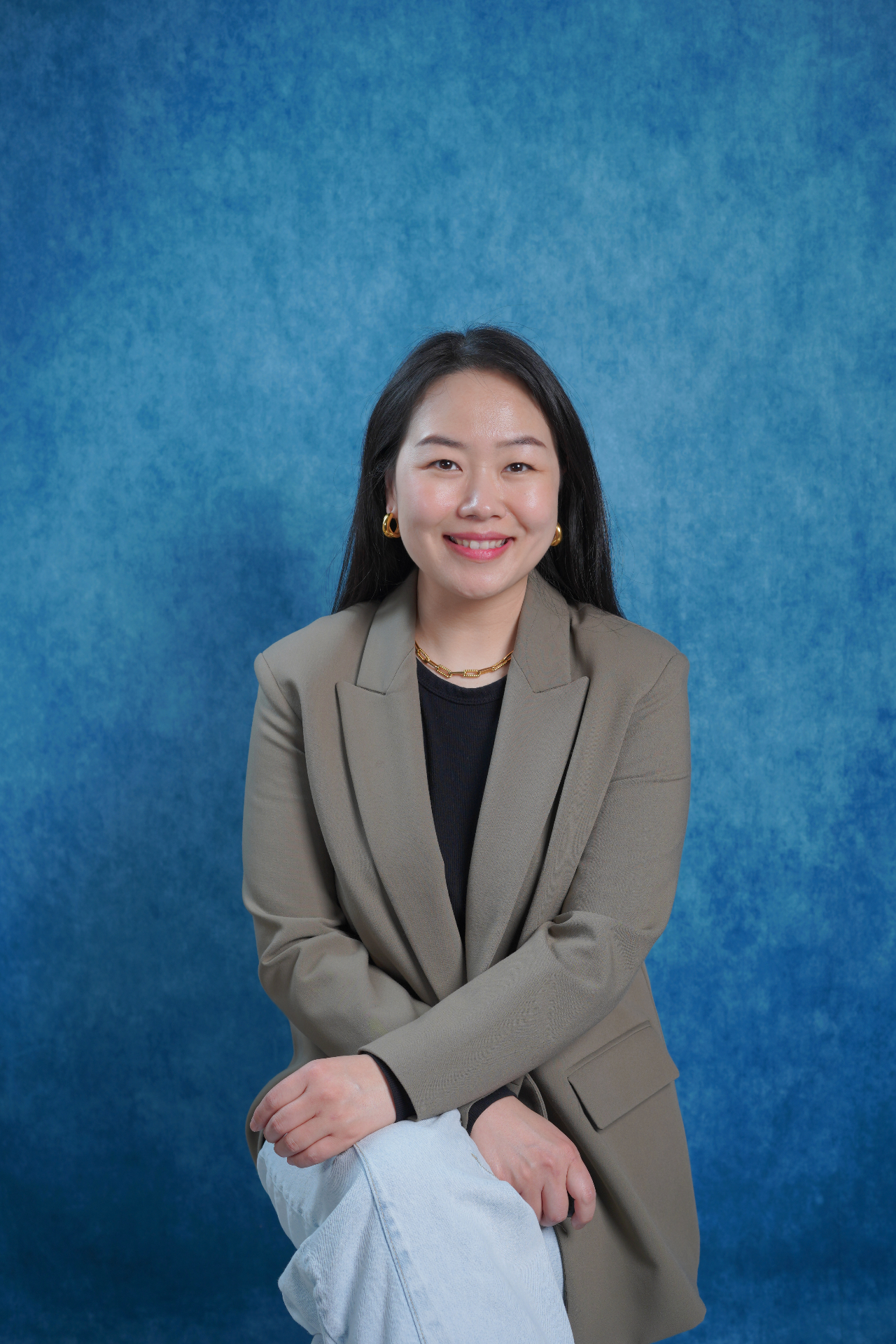 Professional headshot of a woman in a blazer on a blue backdrop